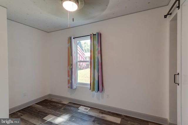 unfurnished room featuring a barn door, dark hardwood / wood-style flooring, and ceiling fan