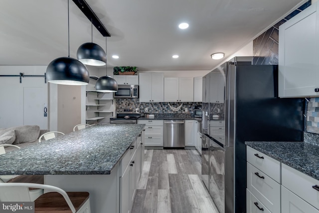 kitchen with appliances with stainless steel finishes, light hardwood / wood-style floors, white cabinetry, a barn door, and a kitchen island