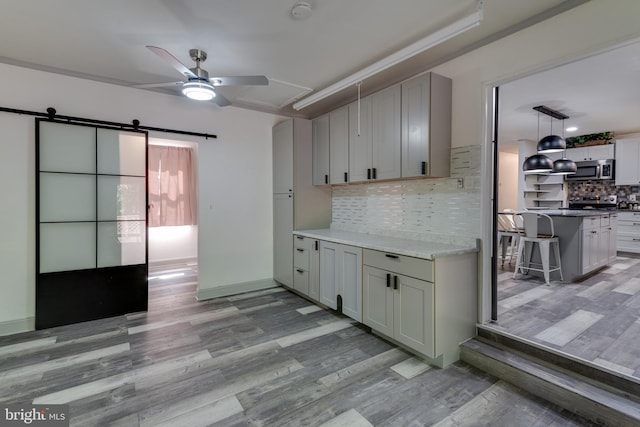 kitchen with a barn door, backsplash, light hardwood / wood-style floors, and ceiling fan