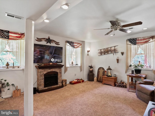 carpeted living room featuring ceiling fan and a stone fireplace