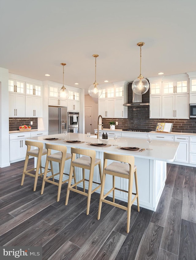 kitchen featuring a large island, dark wood finished floors, white cabinetry, appliances with stainless steel finishes, and wall chimney range hood