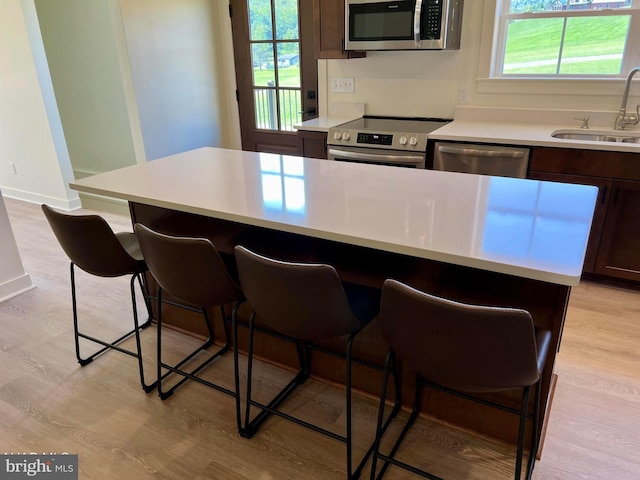 kitchen with appliances with stainless steel finishes, a kitchen bar, plenty of natural light, and light hardwood / wood-style floors