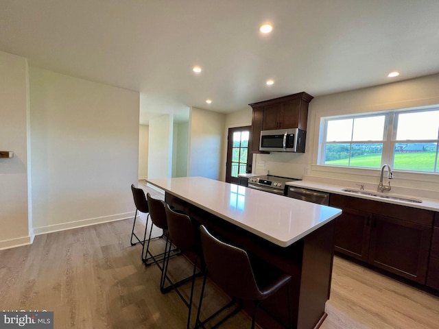 kitchen featuring light hardwood / wood-style floors, a center island, stainless steel appliances, sink, and a breakfast bar