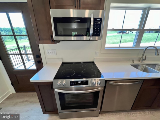 kitchen with appliances with stainless steel finishes, light hardwood / wood-style floors, sink, and dark brown cabinetry