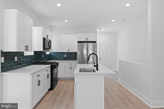 kitchen with black appliances, light wood-type flooring, white cabinetry, and a kitchen island with sink