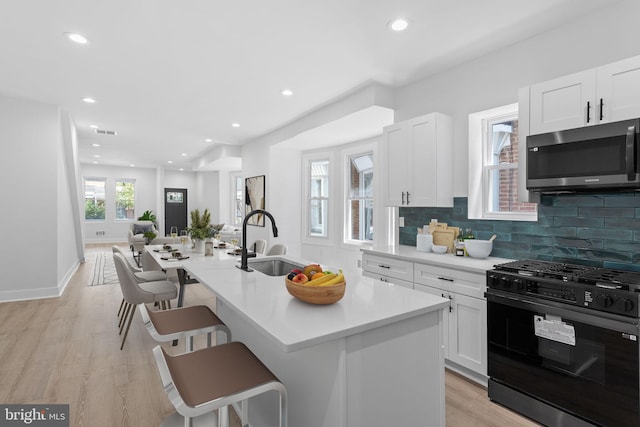 kitchen featuring a kitchen island with sink, light wood-type flooring, white cabinetry, and black gas stove