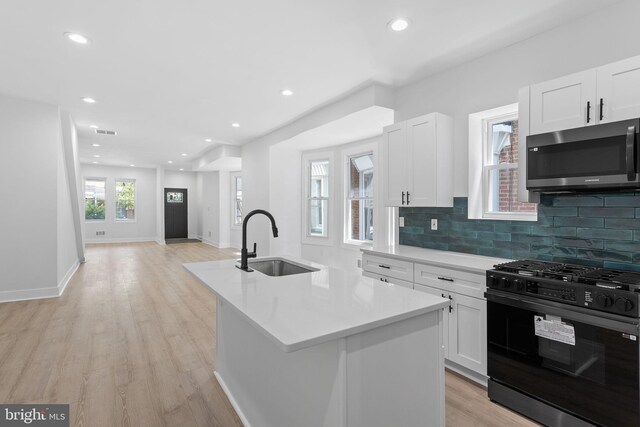 kitchen with gas stove, a kitchen island with sink, sink, white cabinetry, and light wood-type flooring