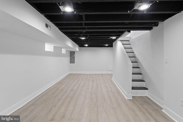 basement featuring electric panel and light hardwood / wood-style floors