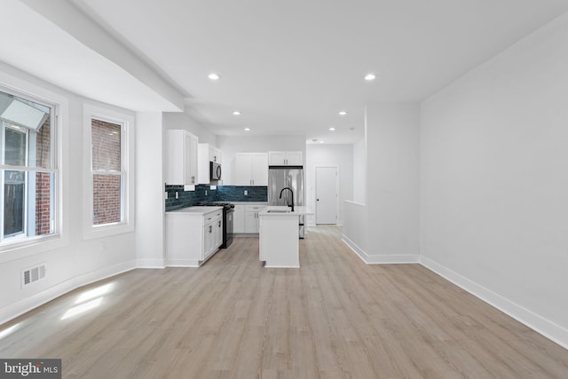 kitchen with light wood-type flooring, black appliances, white cabinetry, and an island with sink