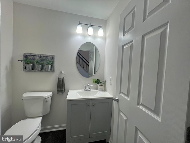 half bathroom featuring vanity, toilet, and baseboards