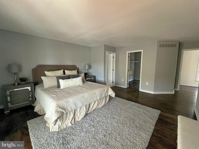 bedroom with baseboards, visible vents, dark wood finished floors, a closet, and a walk in closet