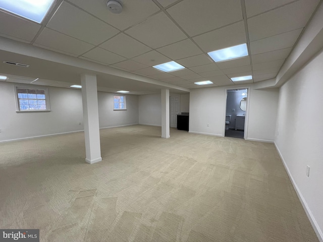 basement featuring a paneled ceiling, baseboards, and light carpet