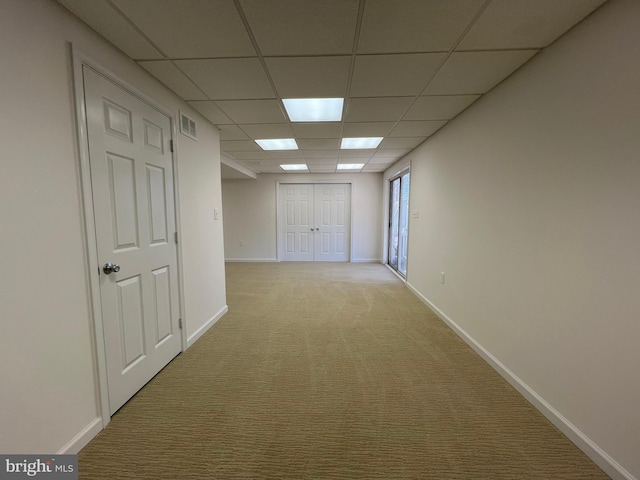 hallway featuring a paneled ceiling, visible vents, baseboards, and light colored carpet