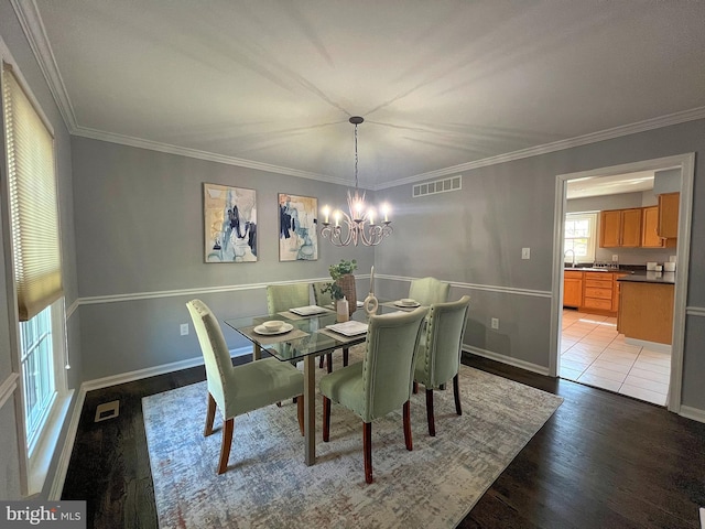 dining space featuring visible vents, light wood-style flooring, an inviting chandelier, and ornamental molding