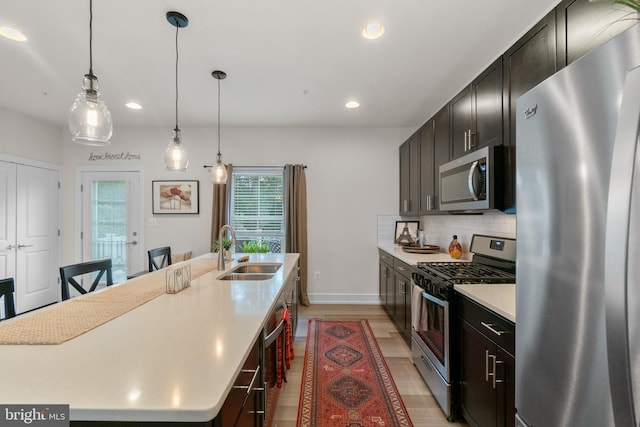 kitchen with an island with sink, a sink, stainless steel appliances, light countertops, and backsplash