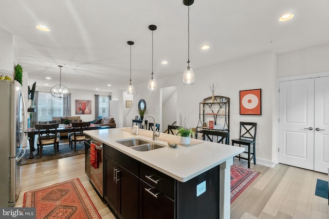 kitchen with stainless steel appliances, light wood finished floors, a sink, and light countertops