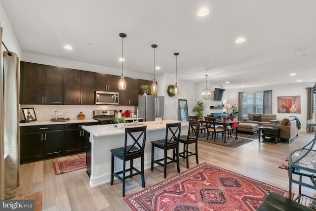 kitchen with appliances with stainless steel finishes, a breakfast bar, light countertops, light wood-type flooring, and backsplash