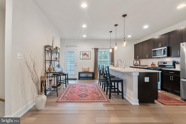 kitchen featuring light wood finished floors, a breakfast bar area, light countertops, decorative backsplash, and appliances with stainless steel finishes