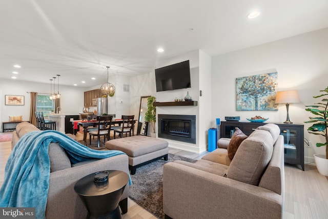 living area with a chandelier, light wood-type flooring, a glass covered fireplace, and recessed lighting