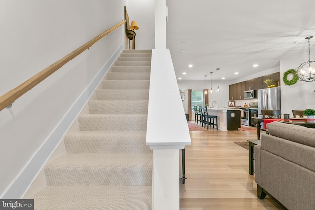 staircase featuring an inviting chandelier, wood finished floors, and recessed lighting