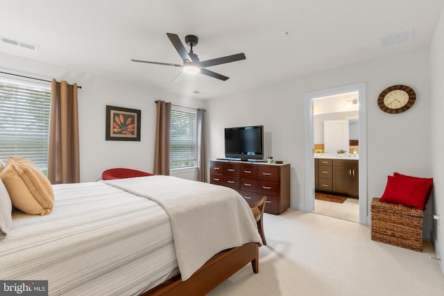 bedroom with a ceiling fan, light colored carpet, visible vents, and ensuite bath