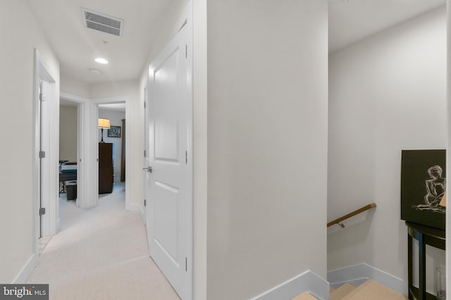 hallway with baseboards, visible vents, light colored carpet, and an upstairs landing