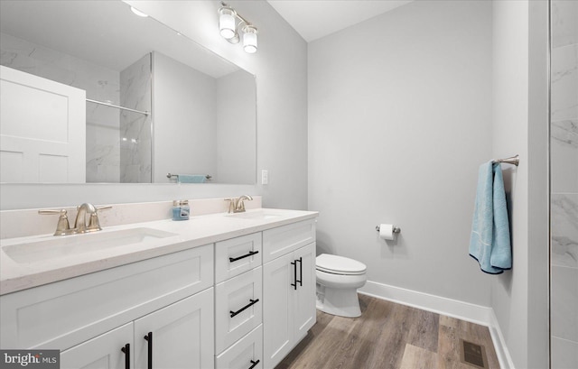 bathroom with wood finished floors, a marble finish shower, double vanity, a sink, and toilet