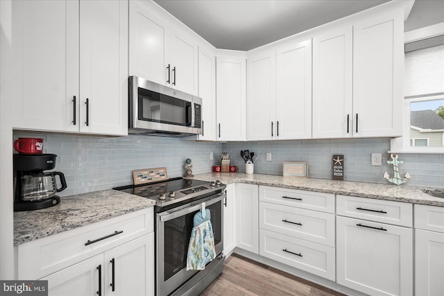 kitchen with light stone countertops, stainless steel appliances, white cabinets, light wood-type flooring, and backsplash