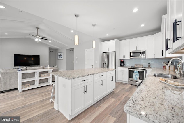 kitchen with light wood finished floors, a kitchen island, a sink, stainless steel appliances, and vaulted ceiling