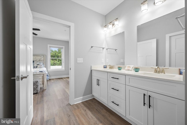 ensuite bathroom featuring wood finished floors, baseboards, double vanity, a sink, and ensuite bathroom