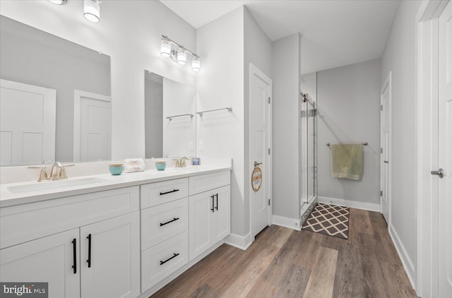 bathroom with double vanity, a stall shower, wood finished floors, and a sink