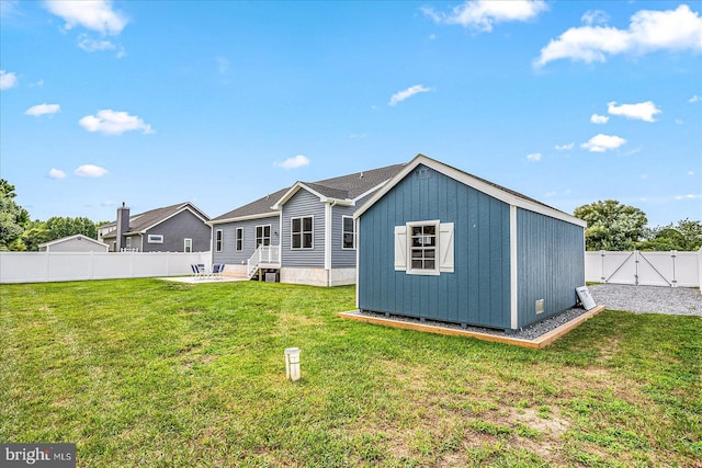 back of house featuring a yard, an outdoor structure, a fenced backyard, and a gate