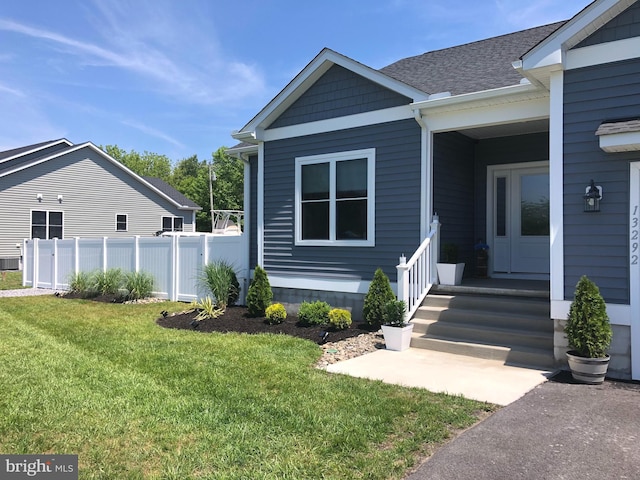 entrance to property featuring a lawn, a shingled roof, and fence