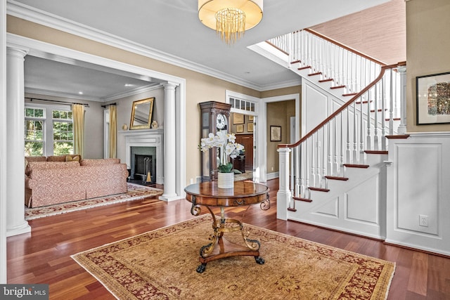 foyer entrance with ornamental molding, decorative columns, a notable chandelier, and dark hardwood / wood-style floors