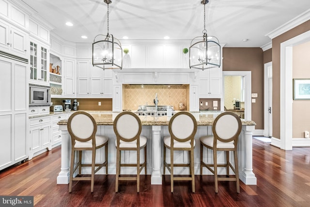 kitchen with stainless steel microwave, a center island with sink, light stone counters, and dark hardwood / wood-style flooring