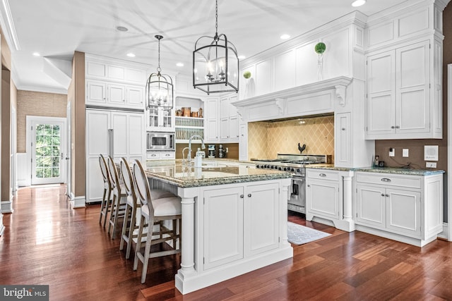 kitchen with white cabinets, built in appliances, dark hardwood / wood-style flooring, and an island with sink