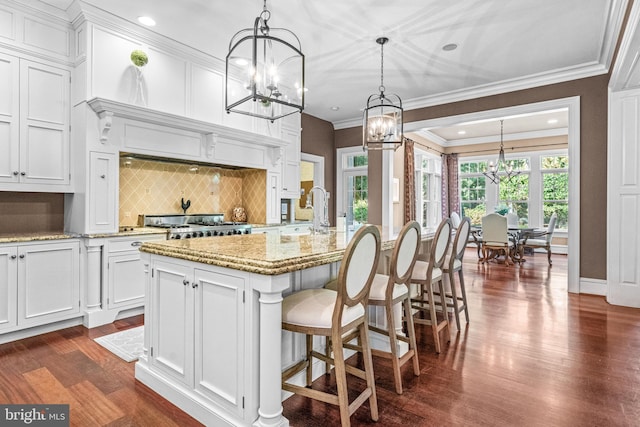 kitchen with dark hardwood / wood-style flooring, hanging light fixtures, white cabinetry, a center island with sink, and backsplash