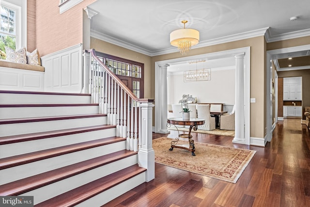 foyer entrance with ornamental molding, decorative columns, a notable chandelier, and dark hardwood / wood-style flooring