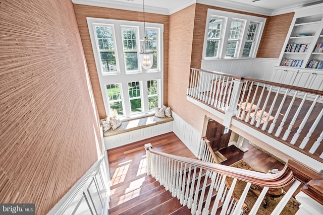 stairs with hardwood / wood-style flooring, crown molding, built in shelves, and an inviting chandelier