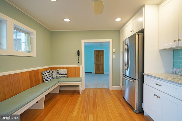 kitchen with light wood-type flooring, white cabinetry, stainless steel refrigerator, a baseboard radiator, and backsplash