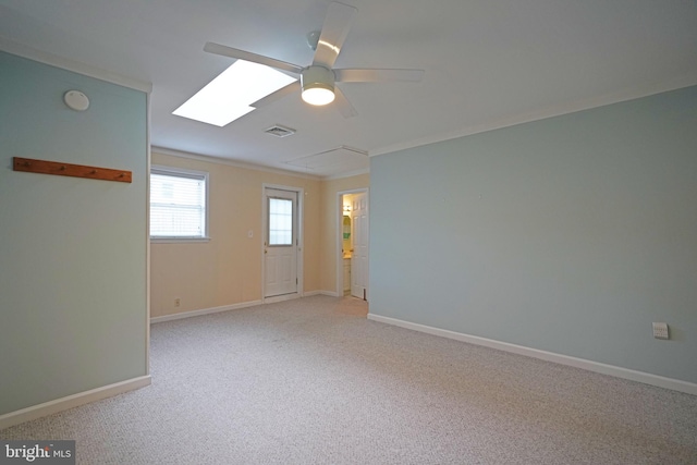 carpeted empty room featuring ceiling fan, a skylight, and ornamental molding