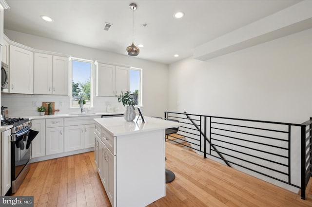 kitchen with light wood-type flooring, appliances with stainless steel finishes, white cabinetry, and a center island