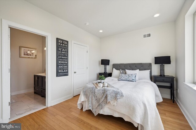 bedroom with connected bathroom and light hardwood / wood-style floors