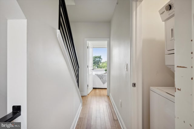 corridor with stacked washer and clothes dryer and light hardwood / wood-style floors