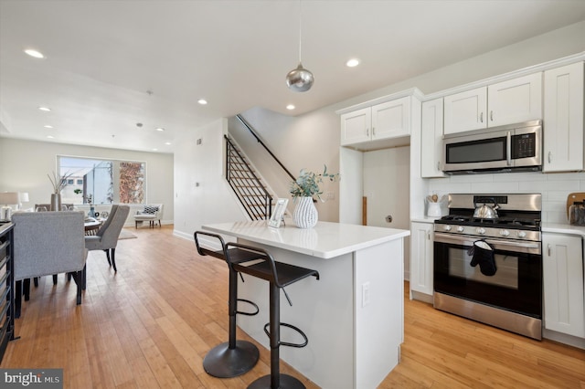 kitchen with light wood-type flooring, pendant lighting, stainless steel appliances, a breakfast bar area, and white cabinets