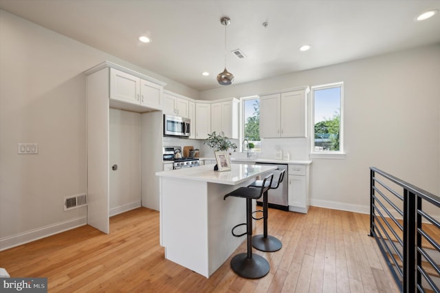 kitchen with appliances with stainless steel finishes, light hardwood / wood-style flooring, a breakfast bar area, and white cabinets