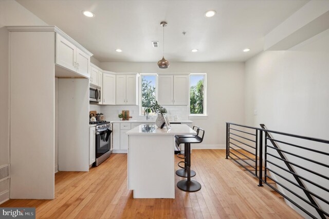 kitchen featuring decorative light fixtures, a center island, stainless steel appliances, light wood-type flooring, and white cabinets