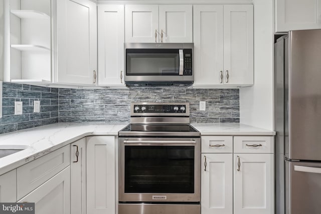 kitchen with light stone countertops, backsplash, stainless steel appliances, and white cabinets