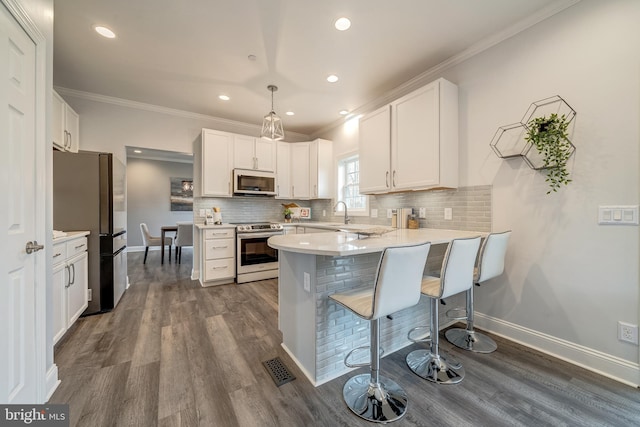 kitchen featuring appliances with stainless steel finishes, dark wood-type flooring, a peninsula, and tasteful backsplash