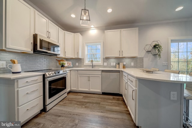 kitchen with a peninsula, a sink, white cabinetry, appliances with stainless steel finishes, and crown molding